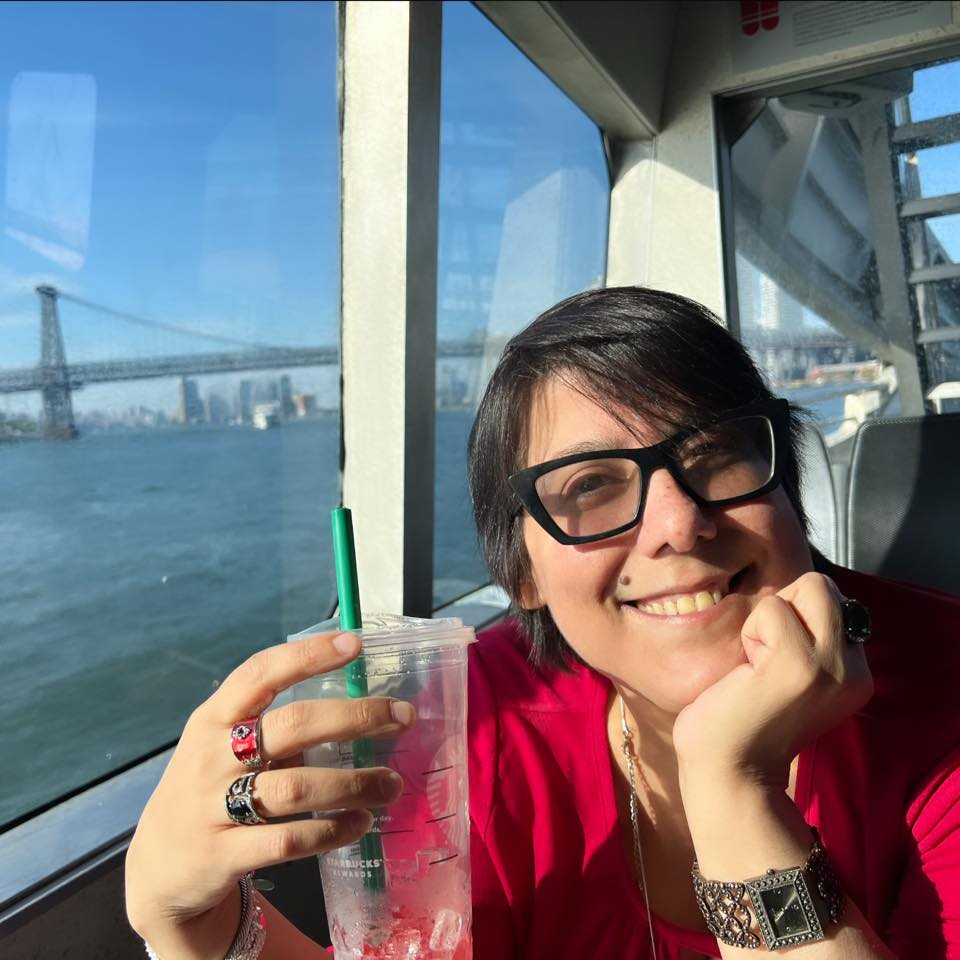 Wearing a red top and holding a Starbucks drink, Christina, her hair short and dark, smiles while riding on a ferry